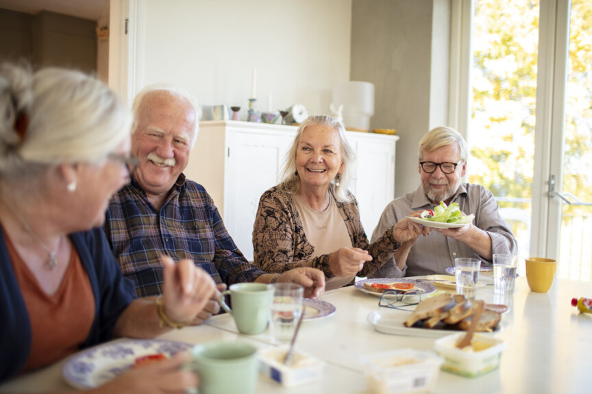 Zu sehen ist eine Gruppe Senioren an einem Tisch die bei einem Frühstück zusammensitzen.