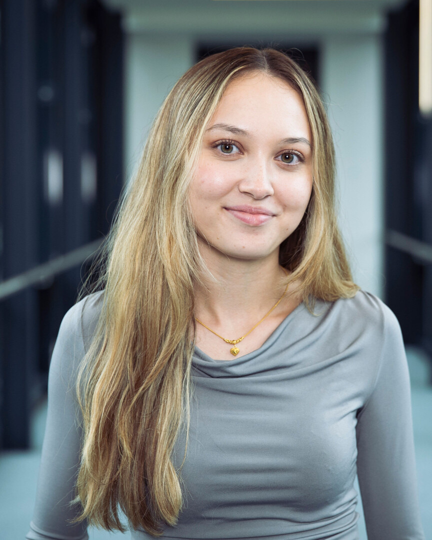 Portraitbild Jasmin Reiner: Junge Frau mit langen blonden Haaren und einem grauen Oberteil.