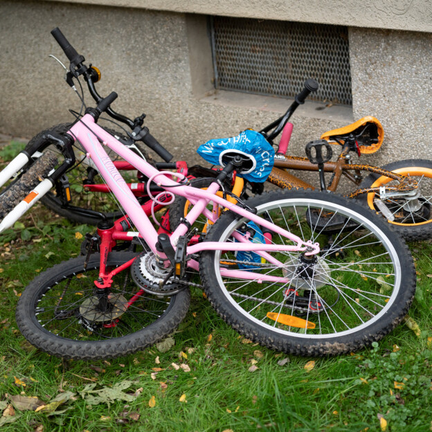 Mehrere Kinderfahrräder liegen im Gras übereinander. Sie wurden offensichtlich länger nicht genutzt.