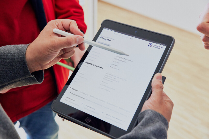Blick über die Schulter einer Person auf ein Tablet. Dort ist die Eingabemaske einer Wohnungsübergabe zu sehen.