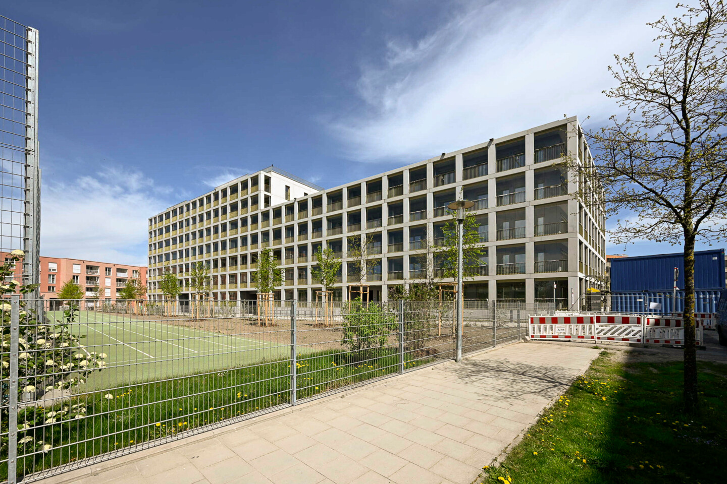 Vor einem mehrstöckigen Wohnhaus ist ein neuer Sportplatz. Drum herum viel Grün.