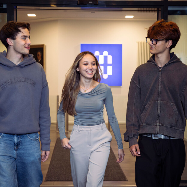 Drei junge Menschen laufen Richtung Kamera. In Hintergrund sieht man das Münchner Wohnen Logo.