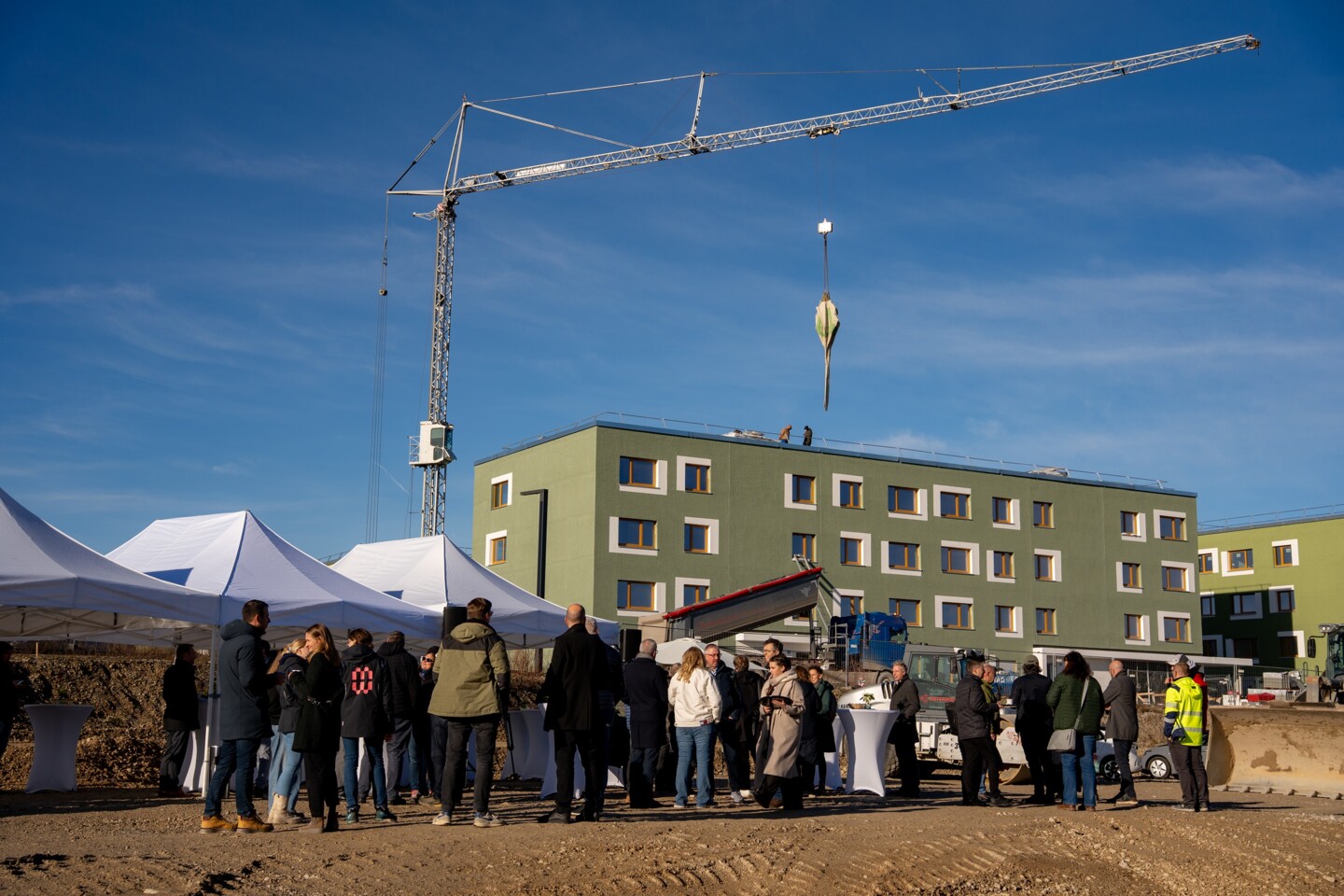Eine Menschengruppe steht vor einem Gebäude mit einem Baukran dahinter.