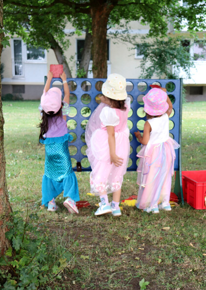 Drei kleine Mädchen spielen in bunt glitzernden Kleidern "Vier gewinnt".