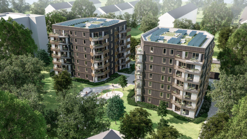 Blick von oben auf zwei mehrstöckige Punkthäuser, die umgeben sind von Bäumen. Dahinter erkennt man weitere Wohngebäude. Der Entwurf zeigt eine Holzfassade mit über Eck liegenden Balkonen und eine Photovoltaikanlage auf dem Dach.