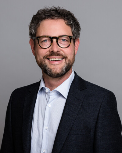 Portraitbild von Steffen Knopp. Mann mit leicht grauem lockigen Haar, Bart und Brille.