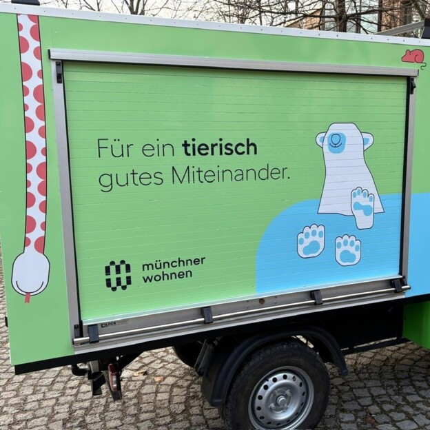 Ein E-Car Auto mit bunter Beklebung in den Münchner Wohnen Farben. neben dem Logo sieht man einen Eisbären und den Spruch: Für ein tierisch gutes Miteinander.
