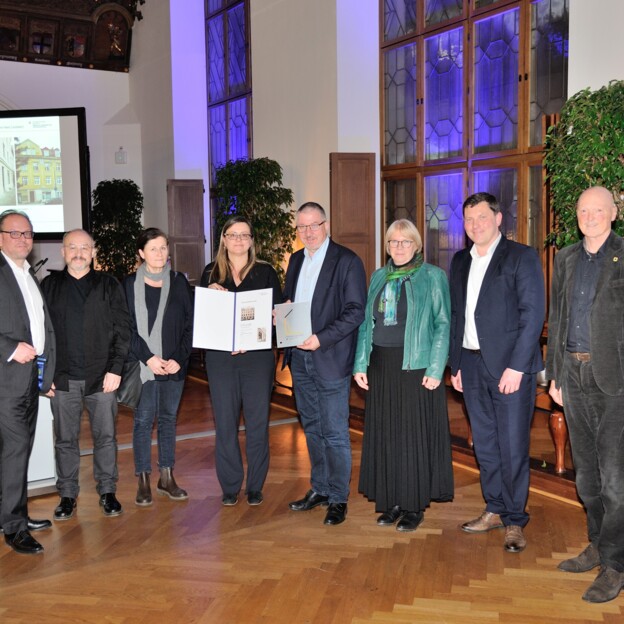 Gruppenbild der Vertreter der Münchner Wohnen und der Stadt München. Auf einer Leinwand im Hintergrund wird ein Foto des ausgezeichneten Hauses gezeigt.