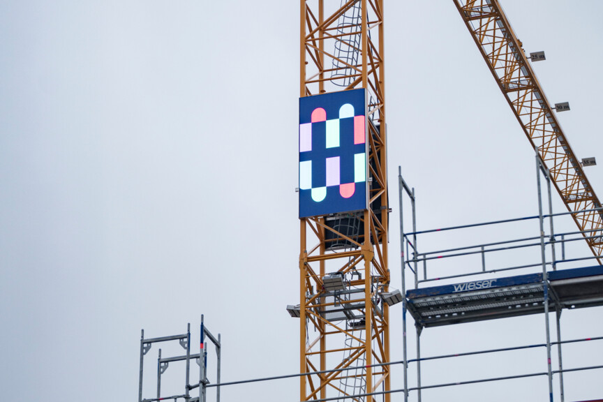 Blick auf einen Baukran an dem das Logo der Münchner Wohnen angebracht ist.