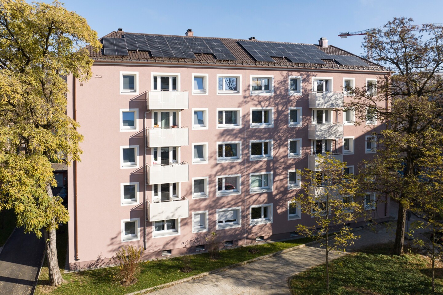 Aufnahme eines modernisierten Wohngebäudes mit Balkonen. Links und rechts davon Baumbestand.