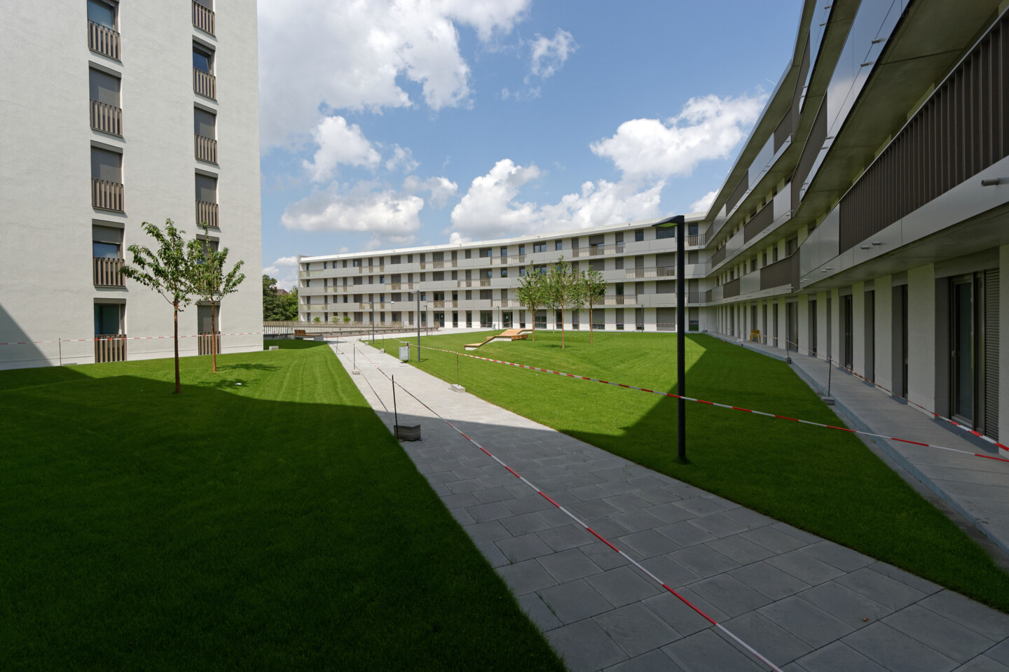 Innenhof des Wohnhauses mit Azubiapartments. Neben großzügigen Rasenflächen sieht man auch Bäume und schön angelegte Gehwege. Die Wohnungen haben nach innen versetzte Balkone.