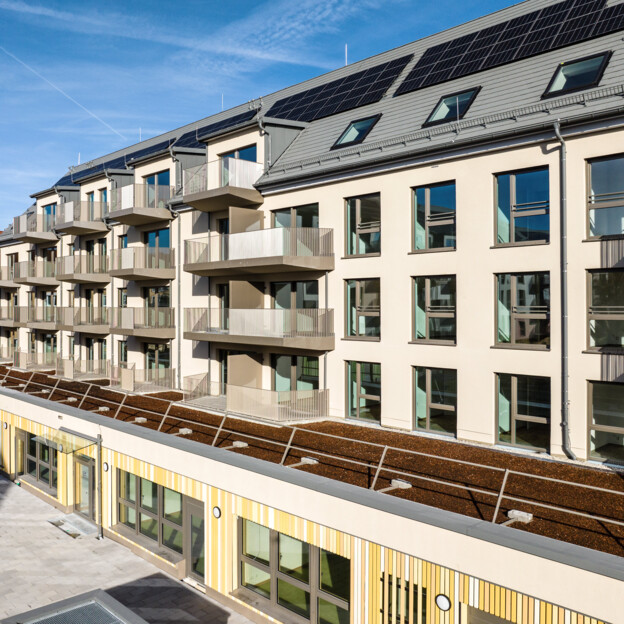 Blick auf ein Neubauwohngebäude mit fünf Stockwerken. Im Erdgeschoss ist eine Kita, darüber liegen Wohnungen.