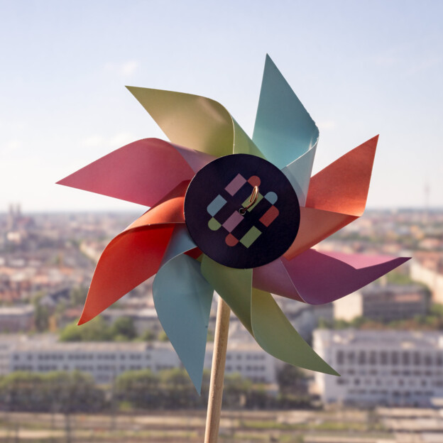 Windrad im Münchner Wohnen Design und im Hintergrund die Stadtsilhouette.