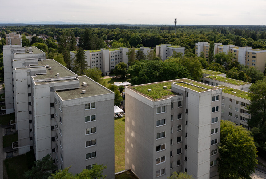 Drohnenaufnahme der Wohnanlage der Münchner Wohnen in Taufkirchen. ein grüner Innenhof mit großem Baumbestand ist umringt von mehreren mehrstöckigen Gebäuden.