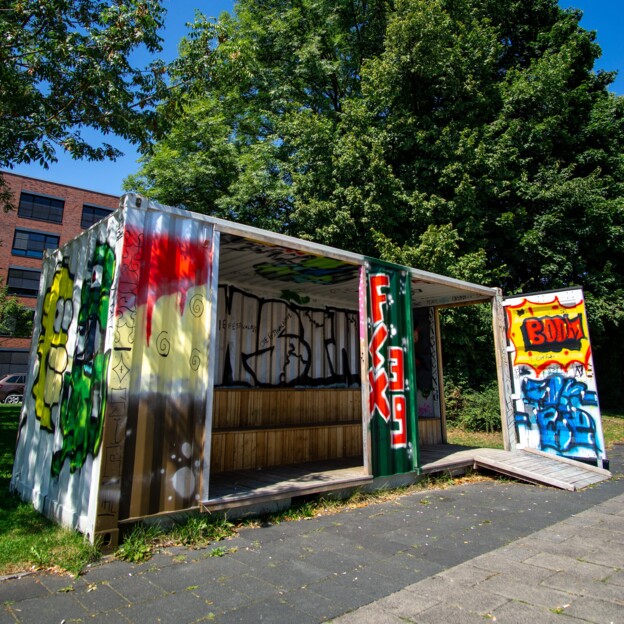 Vorderansicht des Jugendcontainers, der über und über mit buntem Graffiti besprüht ist.