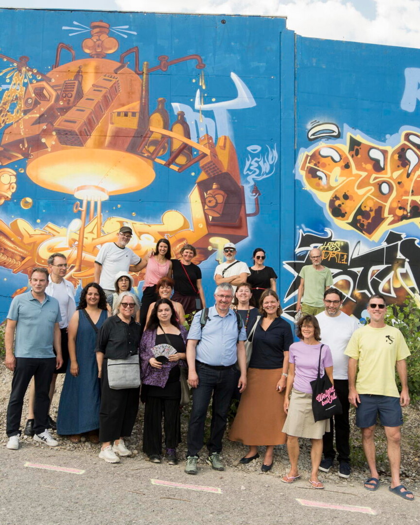 Gruppenbild der Künstler*innen, Geschäftsführung Münchner Wohnen und Projektverantwortlichen vor dem Grafitti.