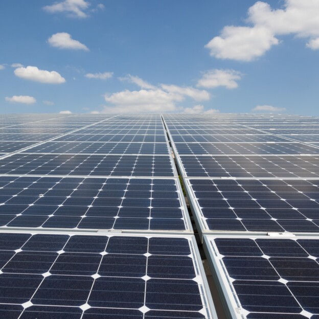Blick auf eine lange Reihe von Photovoltaikanlagen. Am Ende reicht der Blick in den Himmel.