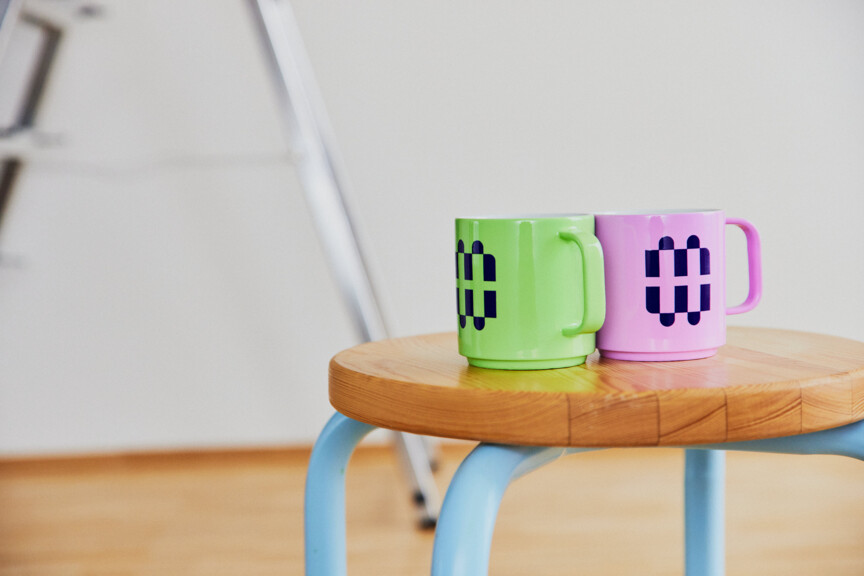 Zwei bunte Tassen im Münchner Wohnen Design stehen auf einem Hocker in einer leeren WOhnunge. Im Hintergrund steht eine aufgestellte Leiter.