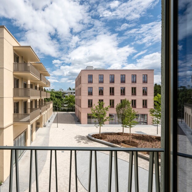 Blick durch das Fenster auf einen Innehof mit Bäumen und die angrenzenden Neubaugebäude.