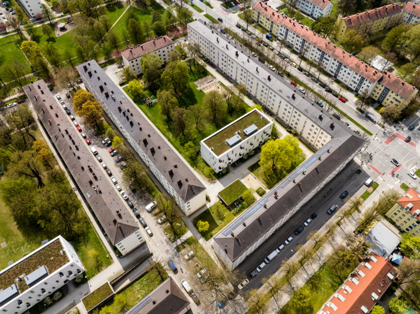 Drohnenaufnahme der Siedlung am Piusplatz. Drei lange Gebäuderiegel umrahmen einen kleineren Riegel. Im Innenhof ist viel Grün.