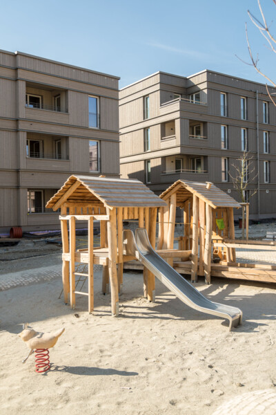 Im Vordergrund ein Spielplatz, im Hintergrund der Neubau in Holzbauweise.