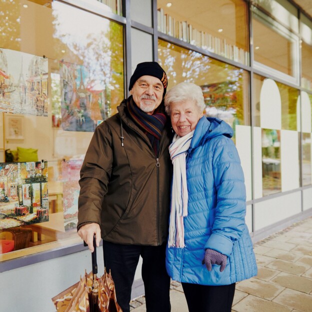 Ein älteres Pärchen steht vor einem Schaufenster des Nachbarschaftstreffs der Münchner Wohnen.