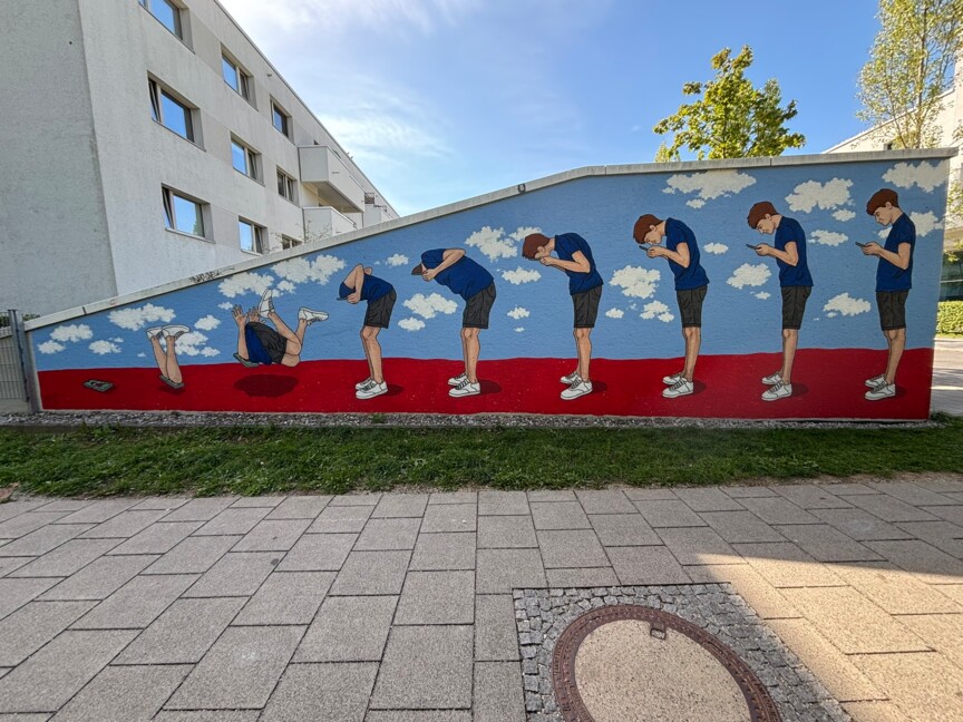 Die Wand einer Garageneinfahrt wurde bemalt. Zu sehen ist ein Mensch der sich immer weiter in sein Smartphone vertieft und am Ende hineinfällt.