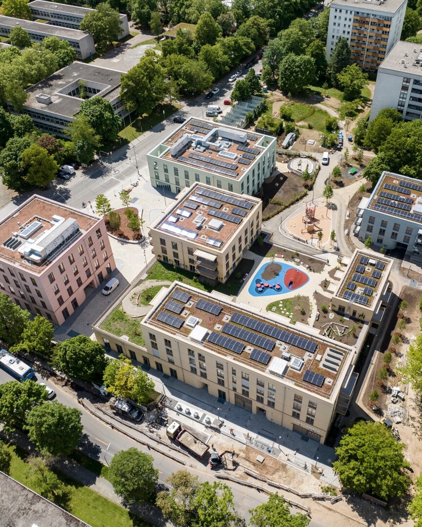 Drohnenaufnahme des Quartiers an der Wiesentfelserstraße. Mehrere rechteckige Wohnhäuser sind um einen Innenhof mit Bäumen und Spielplatz gesetzt.