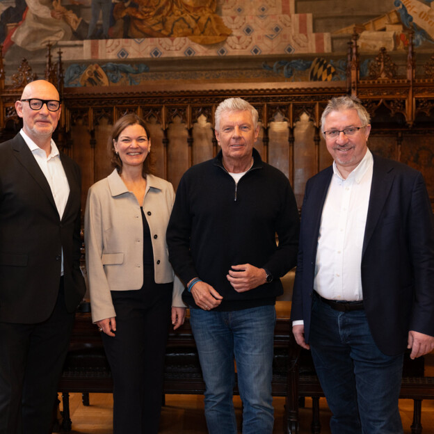 Drei Männer und eine Frau stehen nebeneinander in einem alten Rathaussaal.