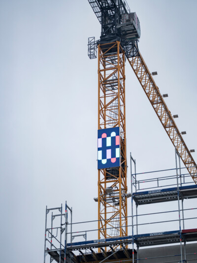 Blick auf einen Baukran an dem das Logo der Münchner Wohnen angebracht ist.