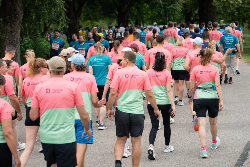 Viele Menschen im Laufshirt mit Münchner Wohnen Logo gehen einen Weg entlang.