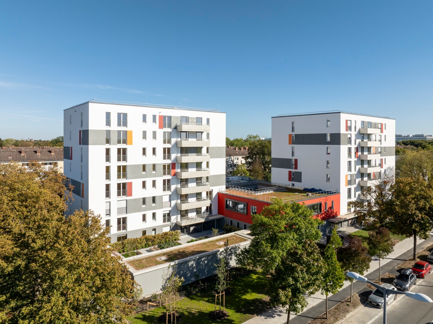 Zwei nebeneinander stehende mehrstöckige Gebäude. Sie sind verbunden durch ein niedrigeres Gebäude zwischen ihnen. Drum herum viele Bäume.