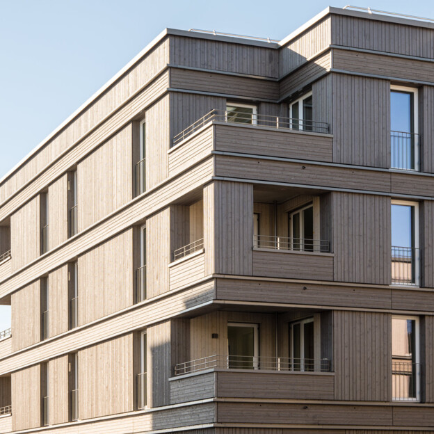 Eckansicht des Holzbaugebäudes mit Blick auf zwei Balkone. Die Holzfassade ist gut zu erkennen.