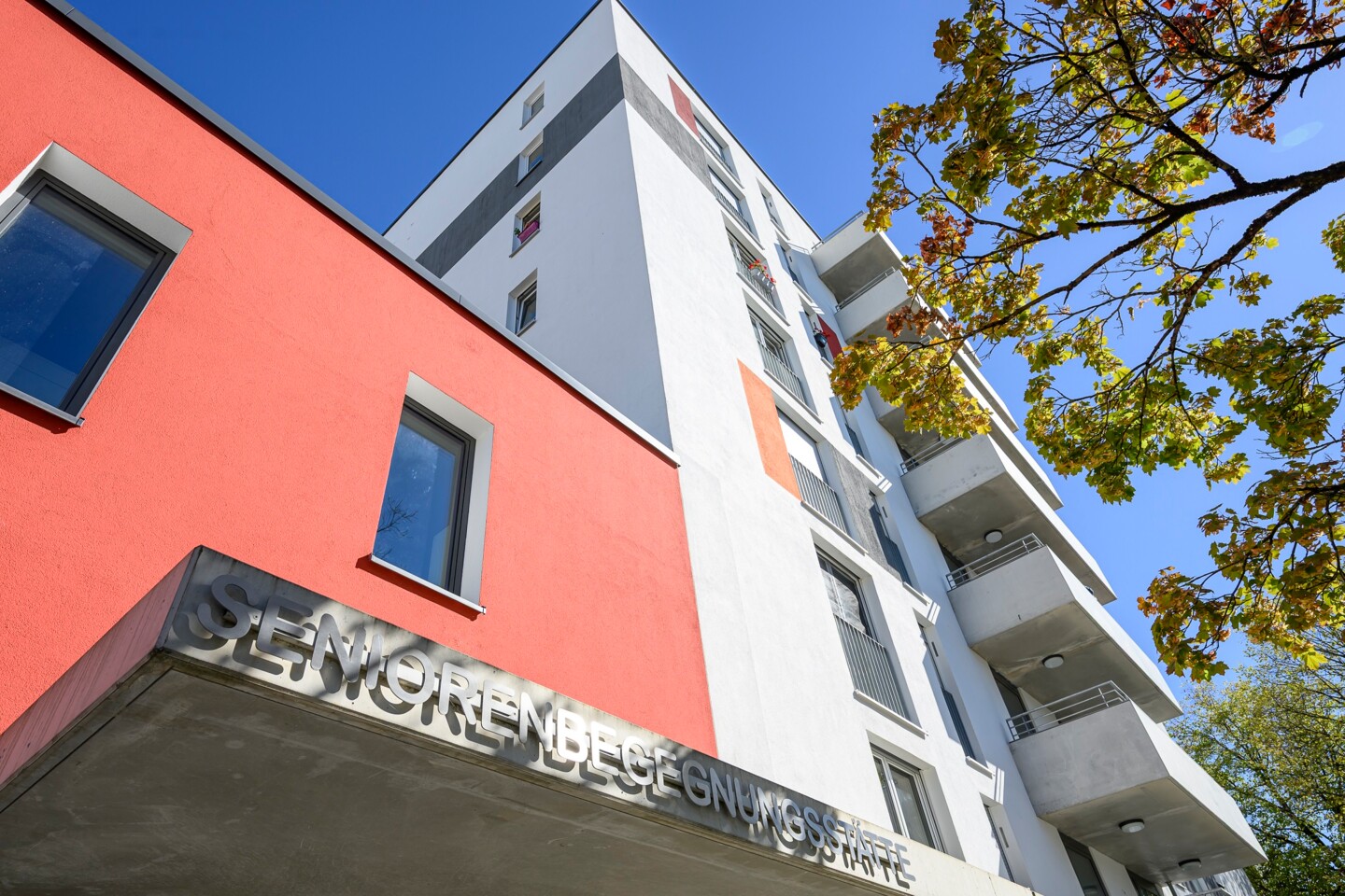 Blick von unten nach oben entlang der weiß und roten Hausfassade. Über dem Eingang steht Seniorenbegegnungsstätte.